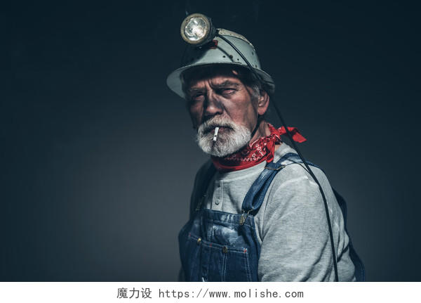 一名高级采矿工人脸上沾满污垢一边抽烟一边直视着灰色背景的相机